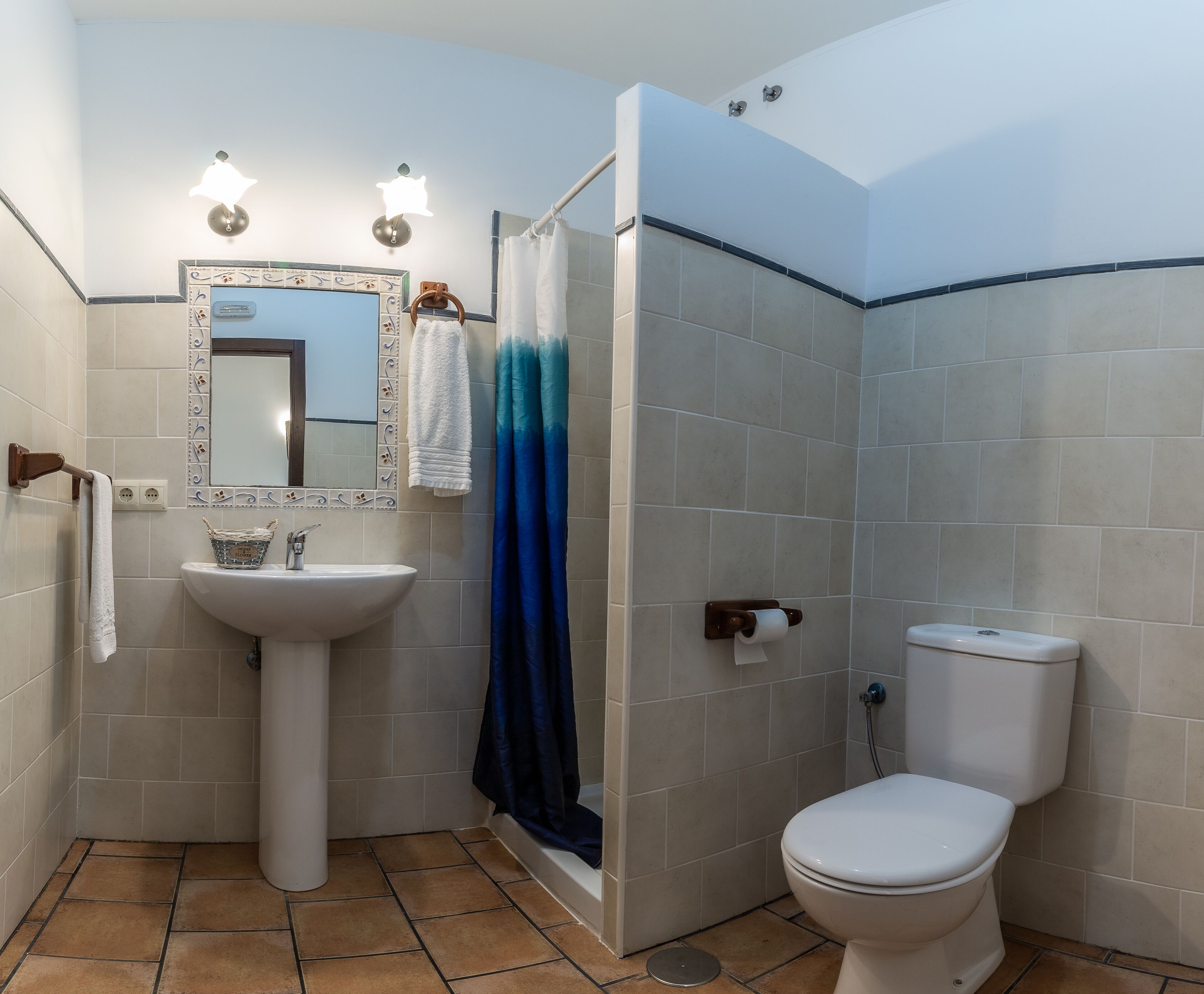A bathroom with a white sink, a toilet, a shower with a blue curtain, and a mirror with lights.