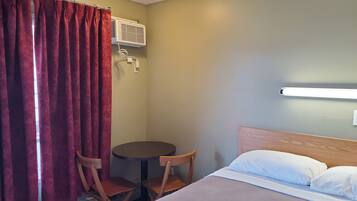 Een hotelkamer met een bed, twee houten stoelen, een klein rond tafeltje, een heater en een airconditioning.