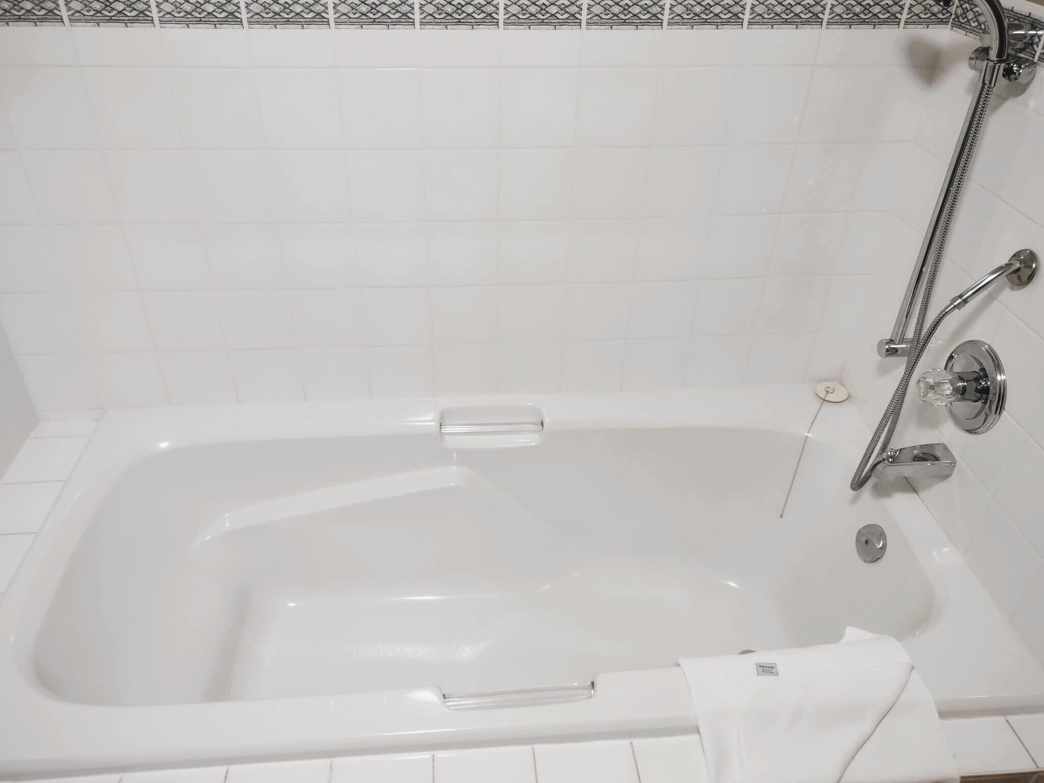 A white bathtub with a handheld showerhead and a glass-enclosed faucet.