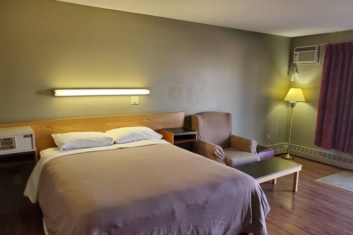 A hotel room with a large bed, a chair, a desk, and a lamp.