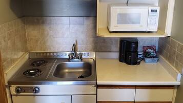 A compact kitchen with a stove, sink, microwave, and a coffee maker.