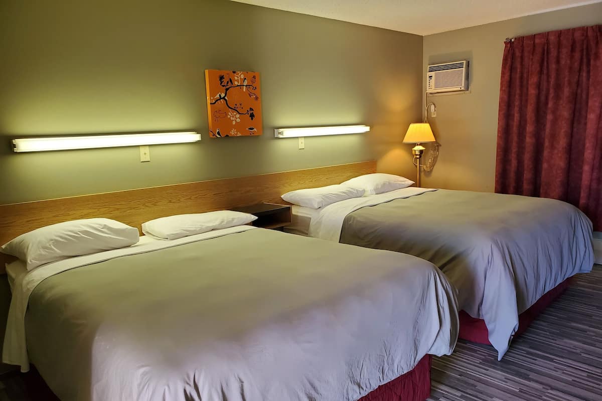 A hotel room with two beds, a wooden headboard, a wall-mounted artwork, a lamp, and a red curtain.
