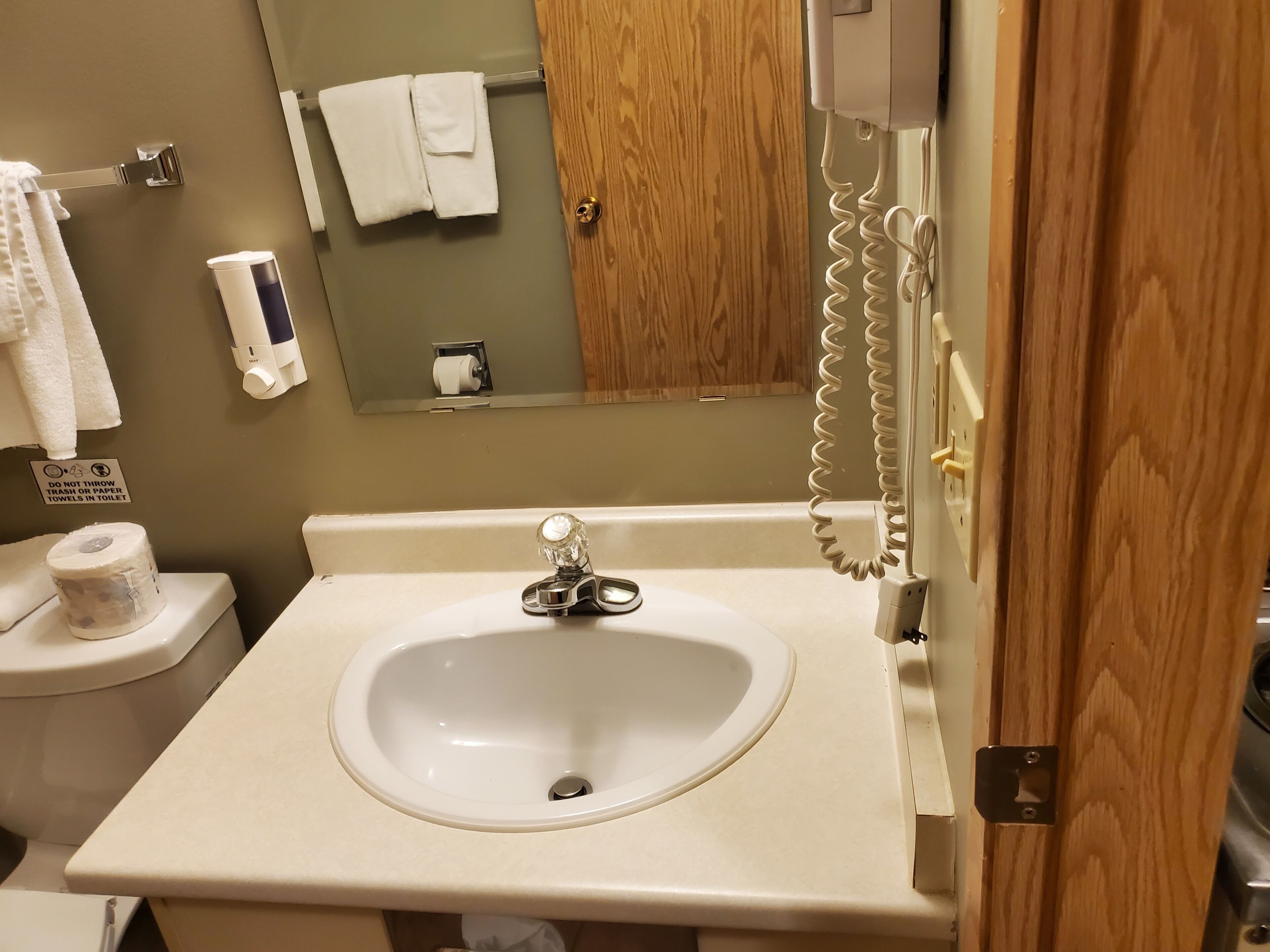 Kylpyhuoneessa on valkoinen pesuallas, wc ja käsienkuivaaja. Kyltissä kehotetaan olemaan heittämättä roskia tai paperipyyhkeitä wc-pönttöön.