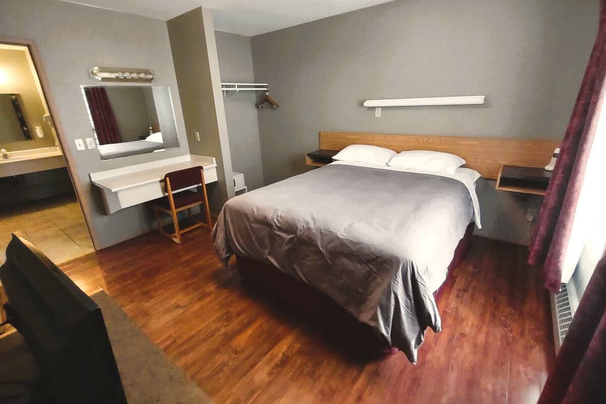 A hotel room with a bed, a desk with a chair, a mirror, and a bedside table.
