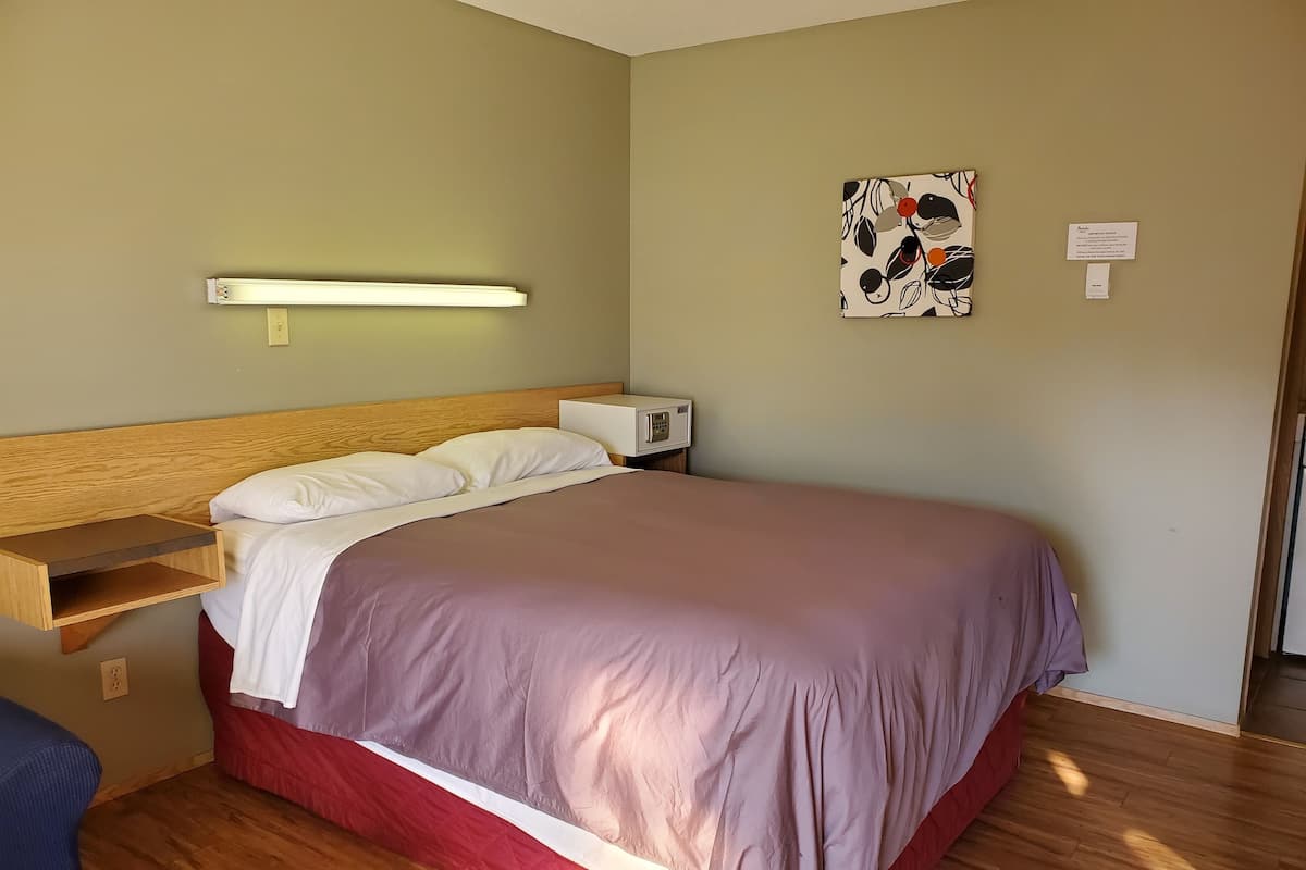 A bedroom with a wooden headboard, a bedside table with a lamp, a bed with a red and purple bedspread, and a wall-mounted artwork.