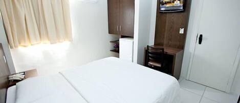 A hotel room with a large bed, a television mounted on the wall, a wardrobe, and a small desk with a chair.