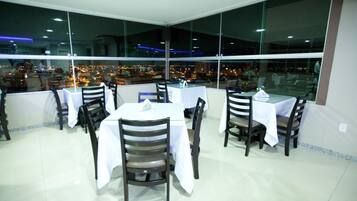A restaurant with tables and chairs, large windows, and a view of the city at night.