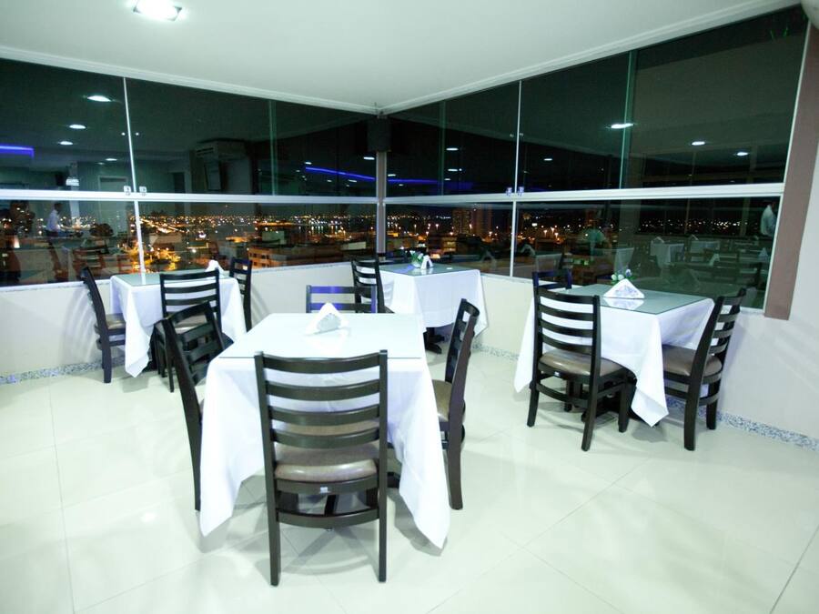 A restaurant with tables and chairs, large windows, and a view of the city at night.