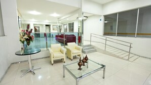 A lobby with a glass coffee table, two white armchairs, a red sofa, and a glass-top table with decorative items. - JB Hotel (Petrolina)