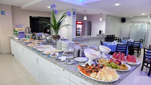 A buffet setup with various food items and a seating area with tables and chairs. - JB Hotel (Petrolina)
