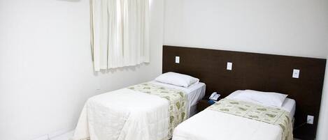Ett hotellrum med två separata sängar, en vit luftkonditioneringsanläggning och ett fönster med gardiner.