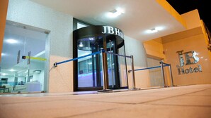 The exterior of JB Hotel with a glass entrance, a revolving door, and a blue security barrier. - JB Hotel (Petrolina)