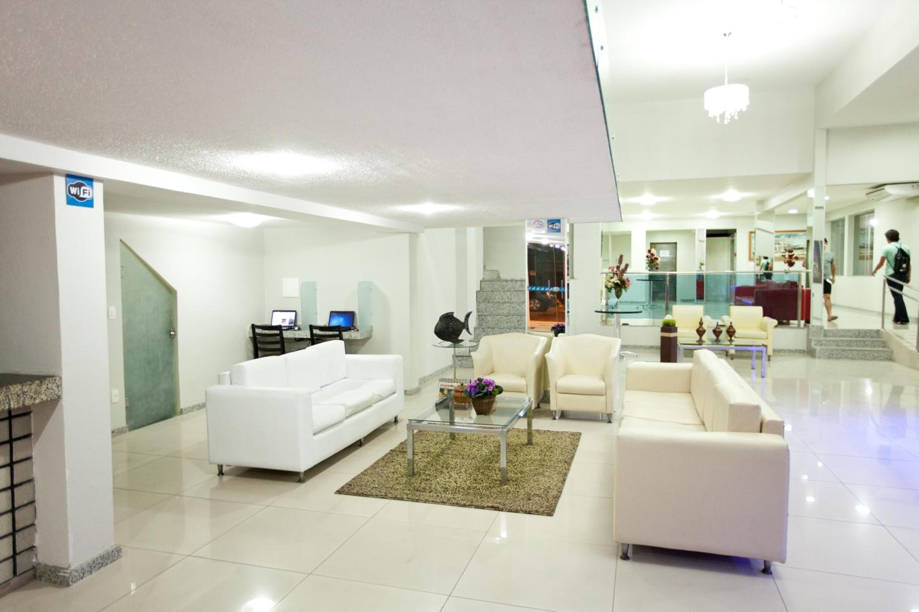 A spacious lobby with a reception desk, white sofas, and a staircase leading to upper floors.