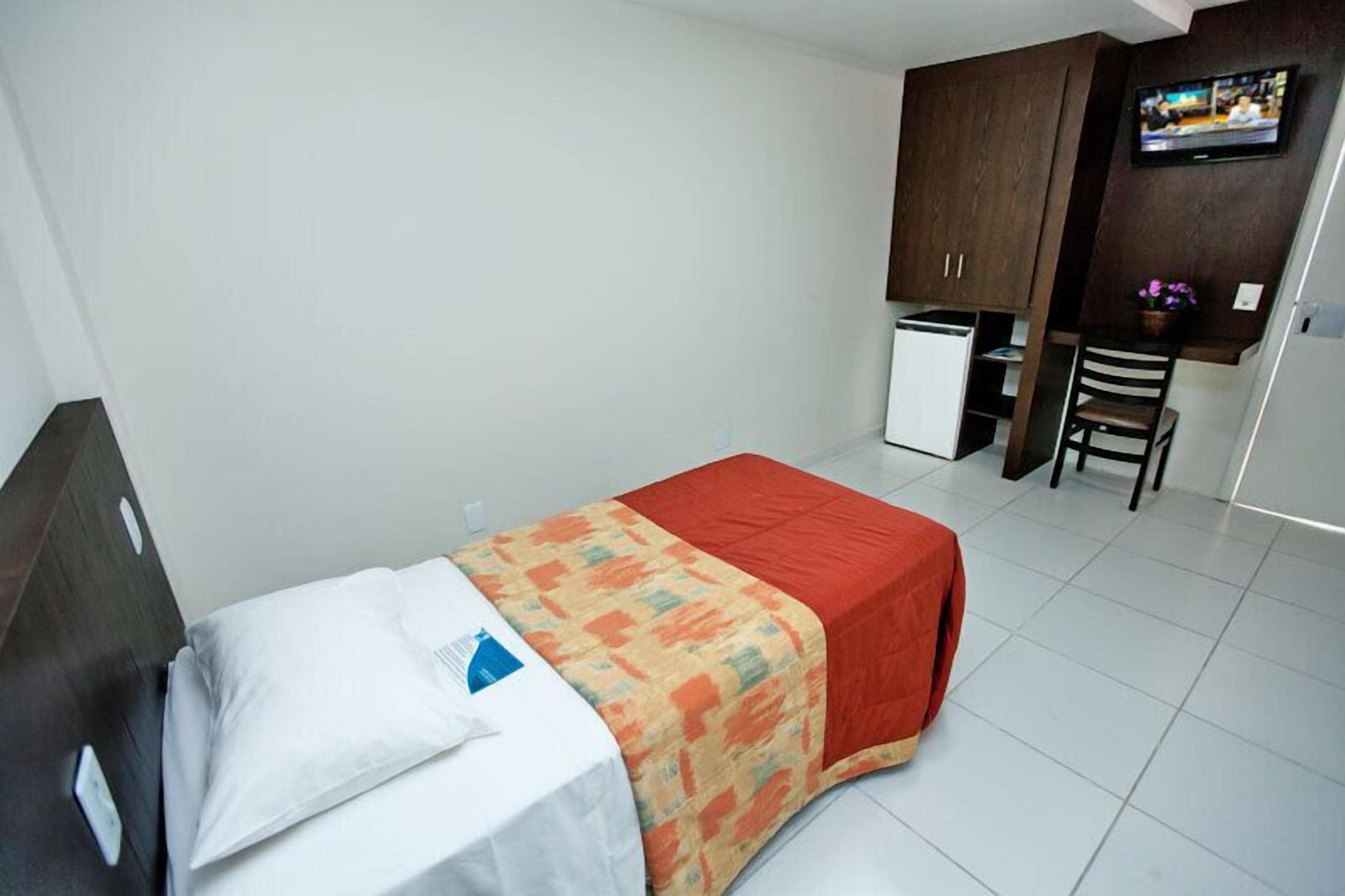 Una habitación de hotel con cama, un escritorio pequeño, televisión y armario.