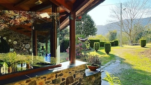 A stone facade with a glass entrance, a wooden roof, and a garden with hedges and a pond. - Casa Rural O Vilar (Ortigueira)
