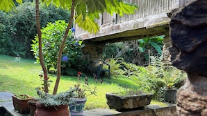 A stone wall with potted plants, a wooden fence, and a rustic building in the background. - Casa Rural O Vilar (Ortigueira)
