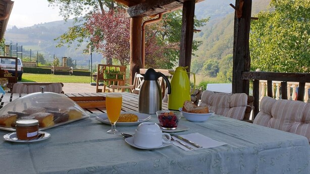 A breakfast table set outdoors with a view of mountains, a wooden deck, and a covered seating area. - La Pumarada de Limés (Cangas del Narcea)