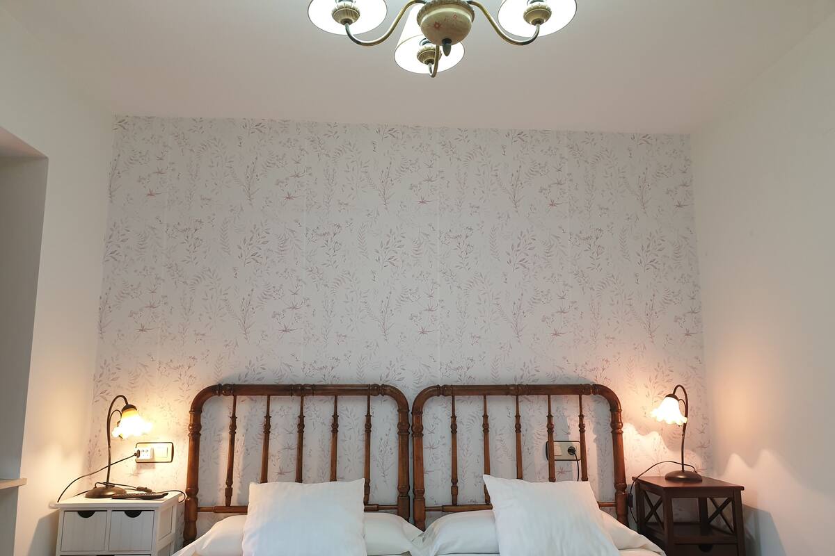 A double bed with a wooden headboard, two bedside tables with lamps, and a floral-patterned wallpaper.
