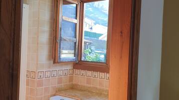 Une salle de bain équipée de toilettes, d’un lavabo et d’une fenêtre donnant sur des bâtiments et de la verdure.