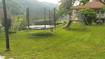 En gräsklädd trädgård med en studsmatta och en gunga.