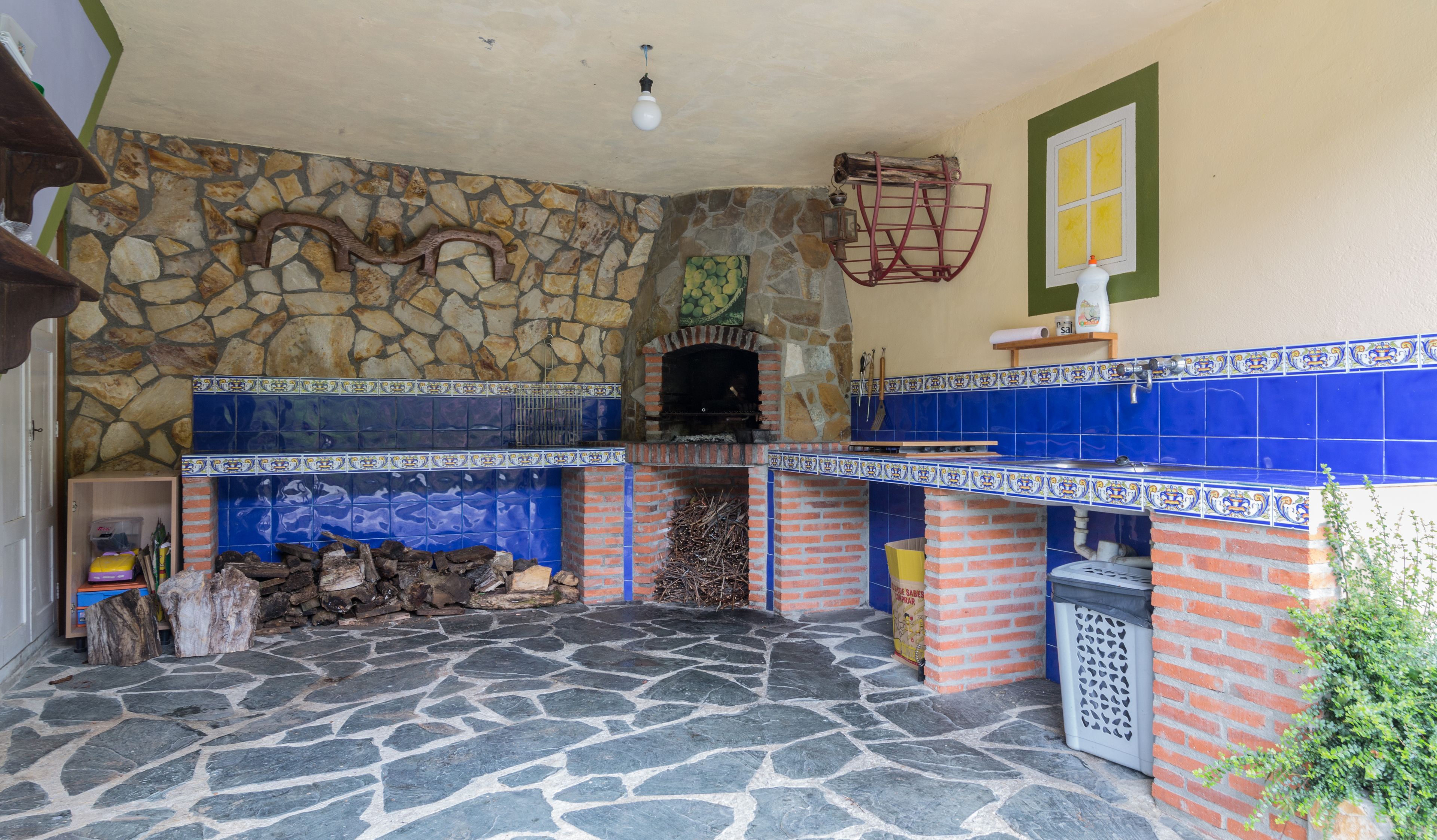 A stone-floored kitchen with a brick oven, blue tiles, and a stone wall.