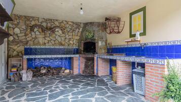A stone-floored kitchen with a brick oven, blue tiles, and a stone wall.