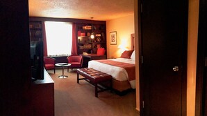 A hotel room with a bed, a desk, a chair, a bookshelf, and a window with curtains. - Hôtel Mingan (Sept-Iles)
