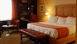 Ein Hotelzimmer mit einem großen Bett, einem Schreibtisch mit Stuhl, einem Bücherregal und einem Fenster mit Vorhängen.