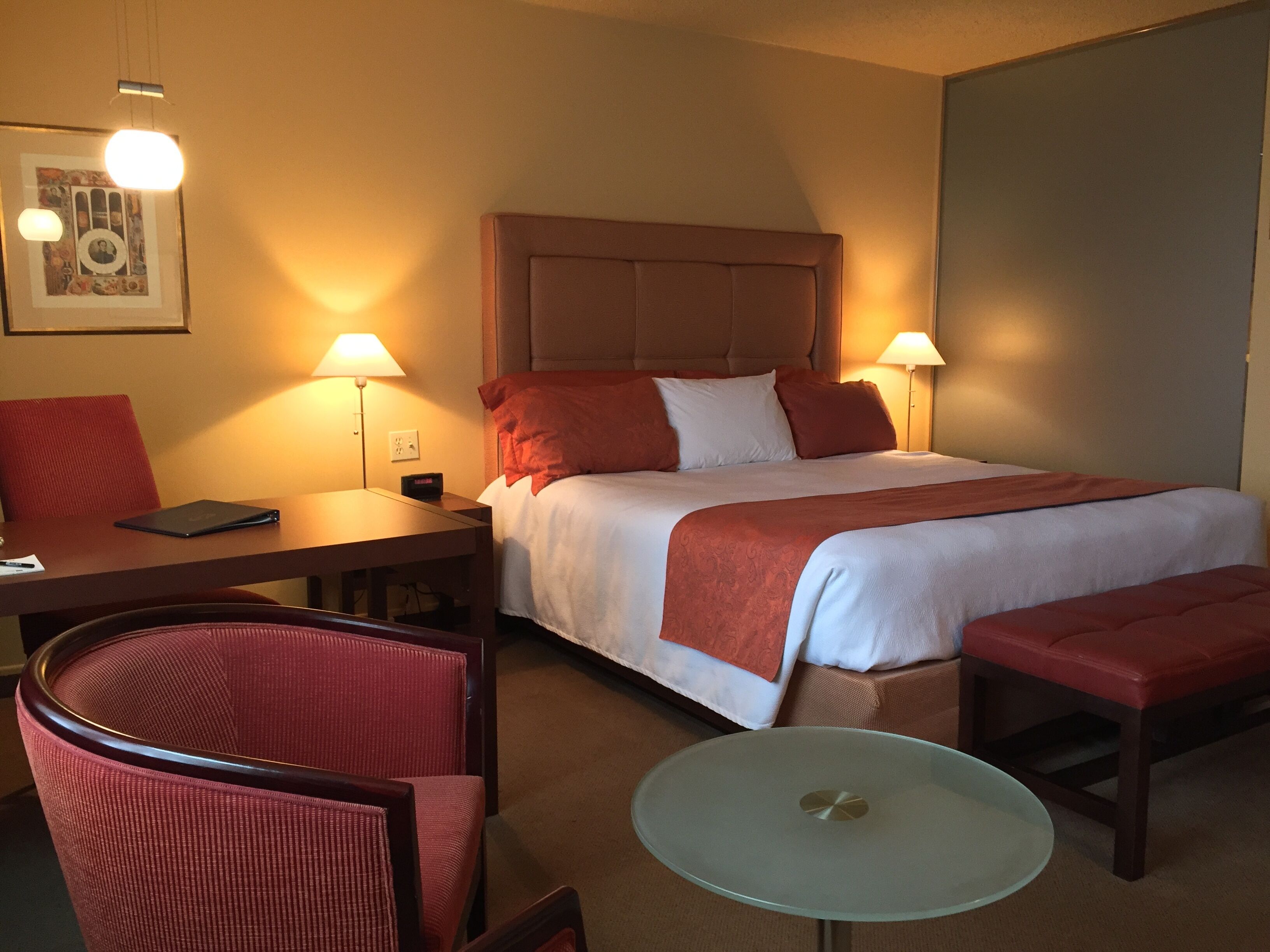 Une chambre d’hôtel avec un lit, deux lampes de chevet, un bureau avec un ordinateur portable, une chaise et une petite table.