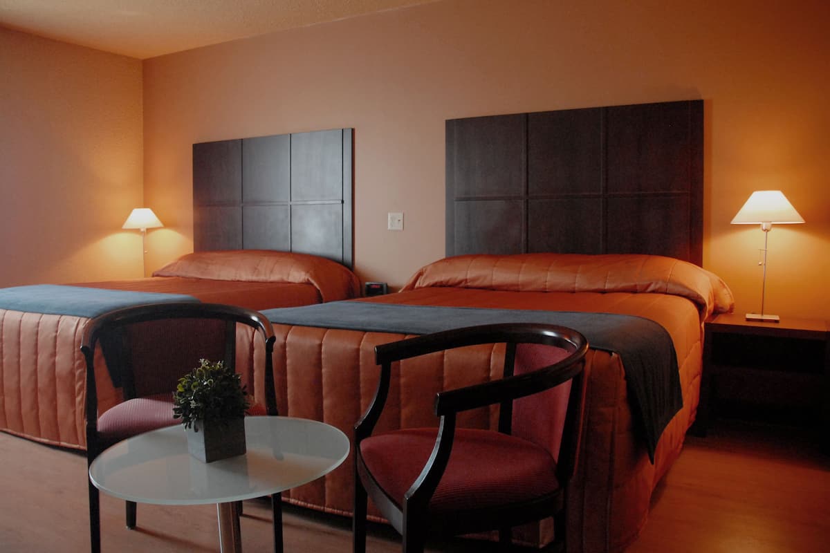 Habitación de hotel con dos camas, una mesita y dos sillas.