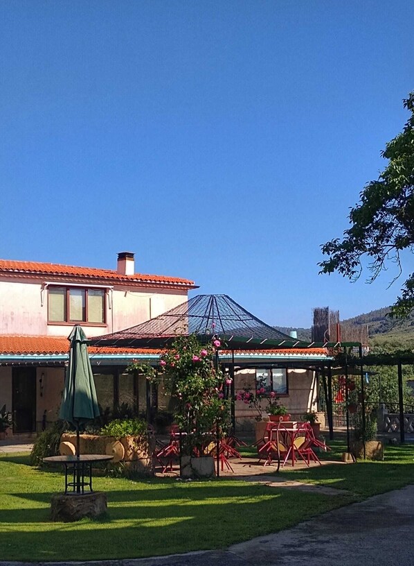 Ein Haus mit einer Terrasse, ausgestattet mit Tisch und Stühlen, umgeben von viel Grün und blauem Himmel.