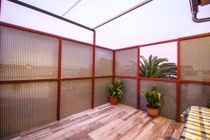 Ein kleiner, abgeschlossener Patio-Bereich mit Holzboden, roten Netzwänden und zwei Kübelpflanzen.