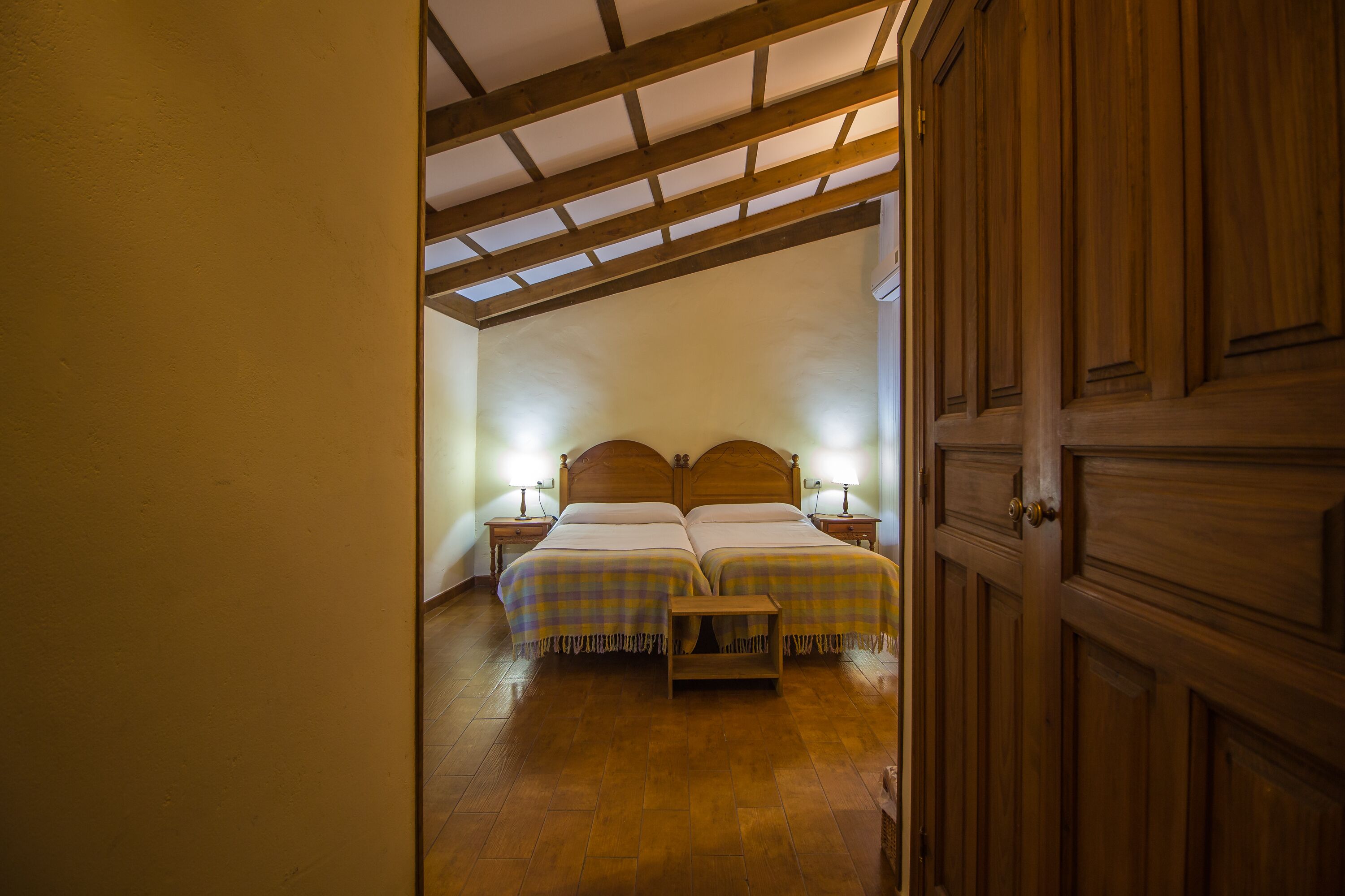 Een slaapkamer met twee bedden, houten hoofdborden en een klein nachtkastje met een lamp.