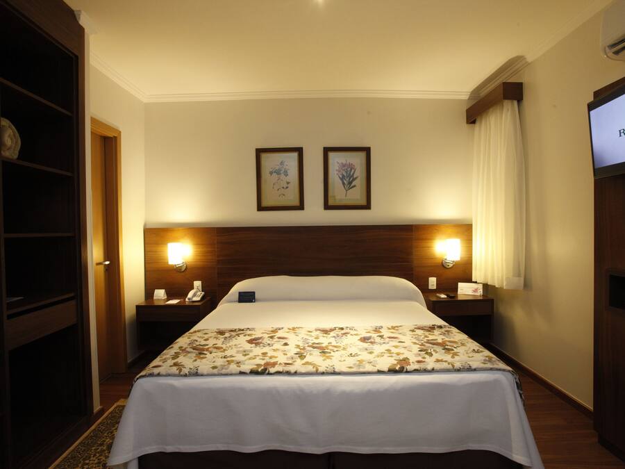A hotel room with a large bed, two bedside lamps, a television, and a wardrobe.