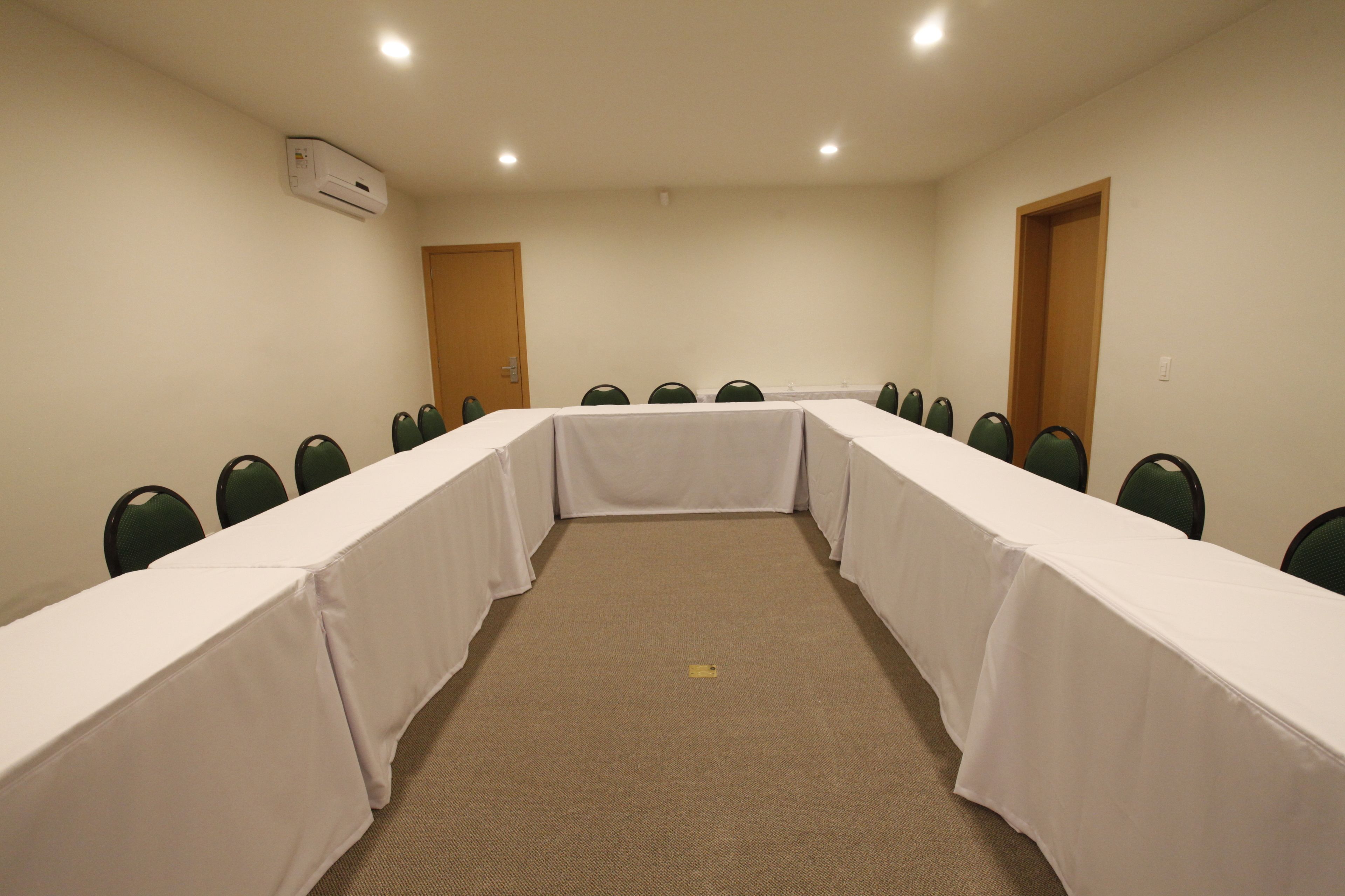 Una sala de conferències amb una taula llarga, cadires verdes i terra amb moqueta.