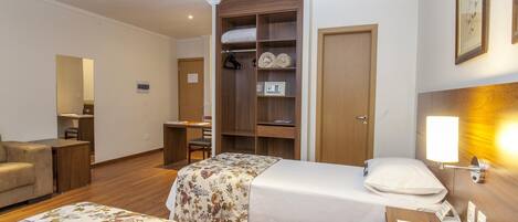A hotel room with two beds, a wooden wardrobe, a desk, and a bedside lamp.