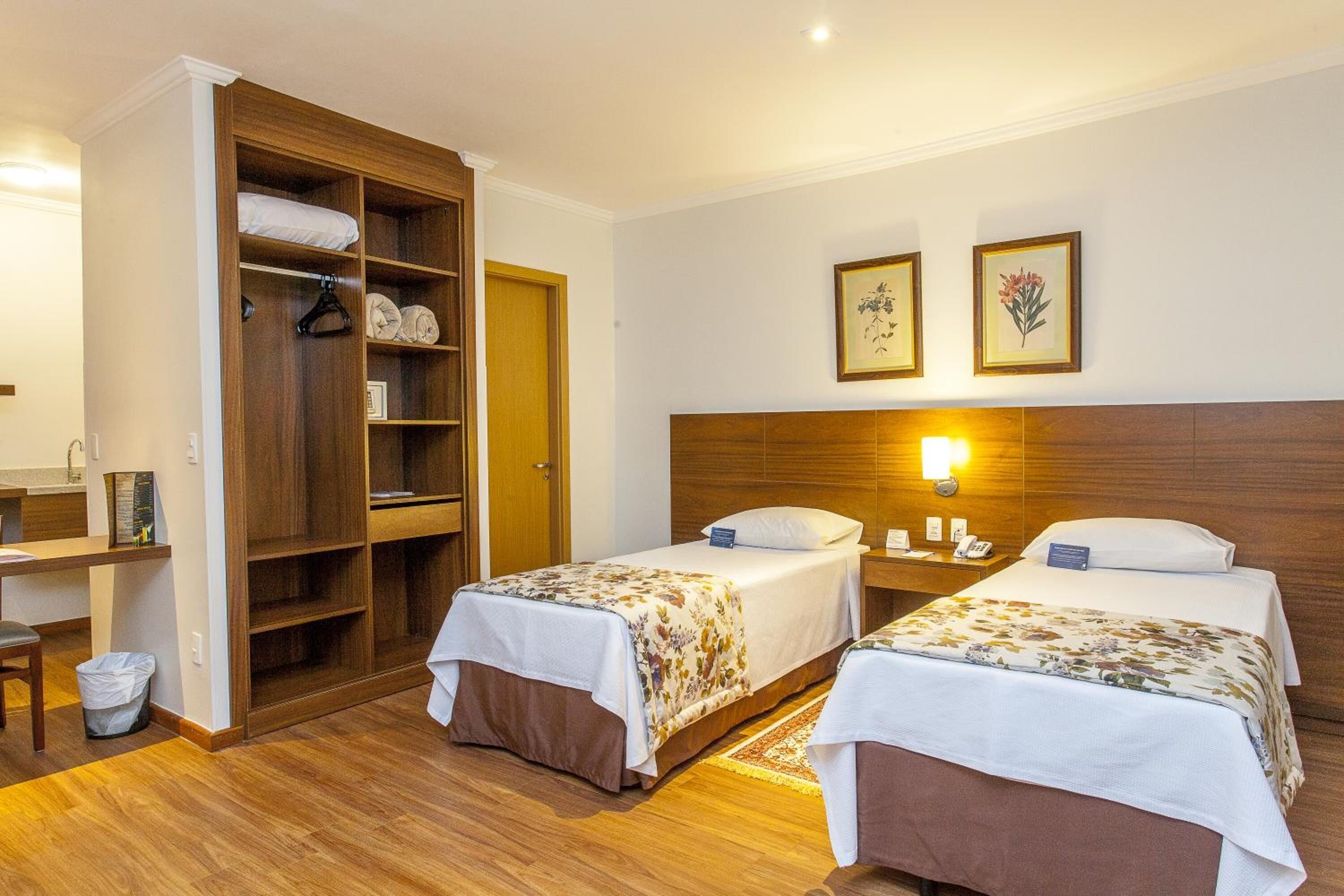 A hotel room with two beds, a wooden wardrobe, a desk, and a nightstand.