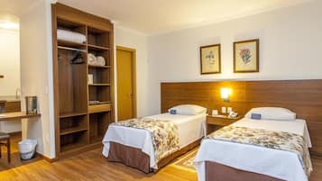A hotel room with two beds, a wooden wardrobe, a desk, and a nightstand.