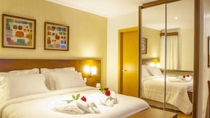 Quarto de hotel com cama grande, um banco de madeira, um espelho e duas luminárias fixadas na parede.