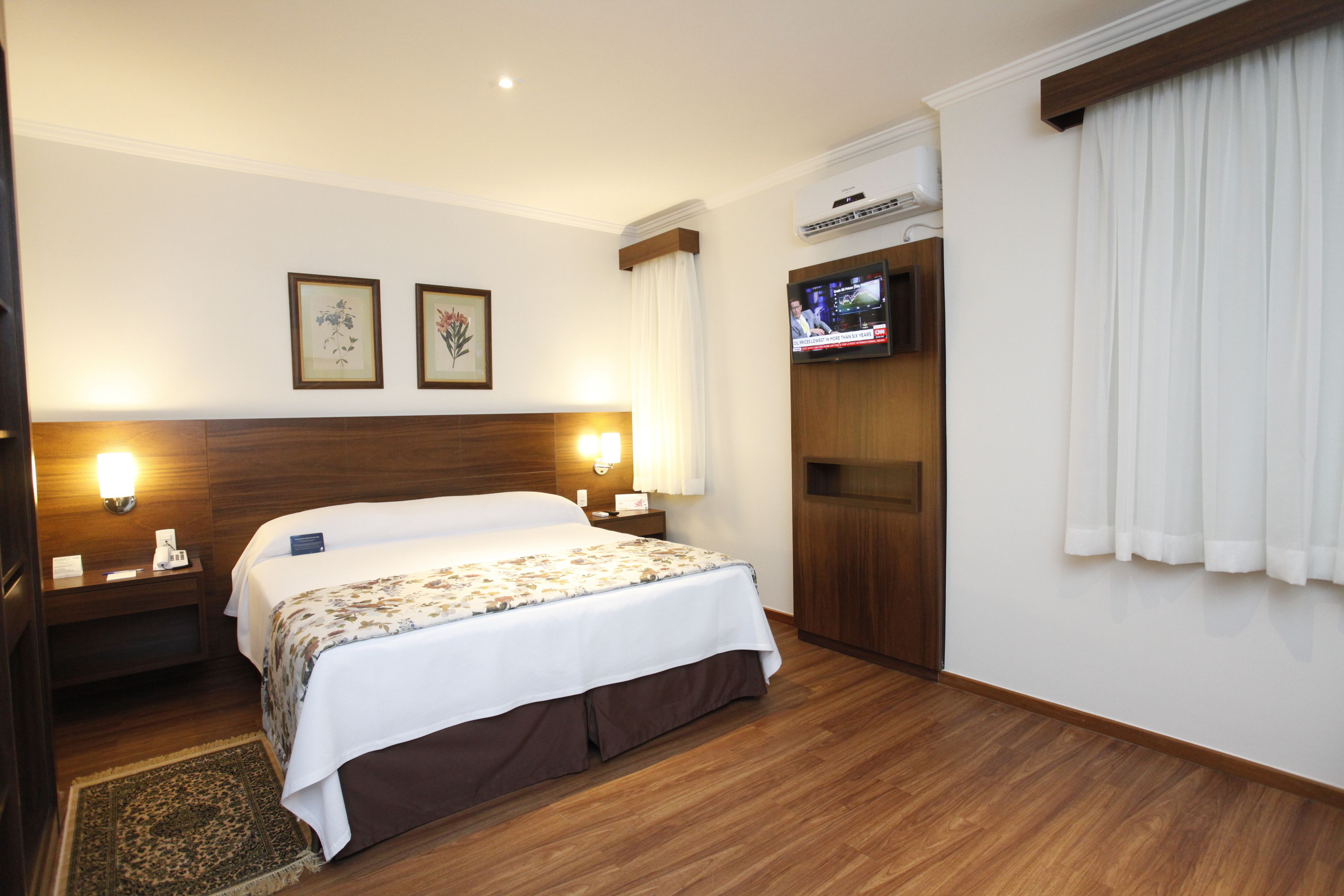 A hotel room with a large bed, two bedside lamps, a flat-screen TV mounted on the wall, and a wooden headboard.