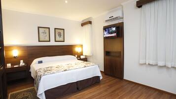 Habitación de hotel con una cama grande, dos lámparas de noche, un televisor de pantalla plana montado en la pared y un cabecero de madera.