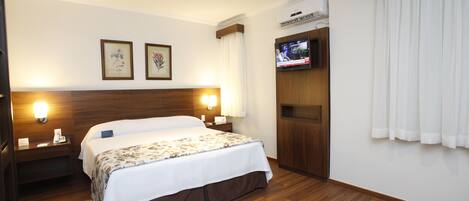 A hotel room with a large bed, two bedside lamps, a flat-screen TV mounted on the wall, and a wooden headboard.