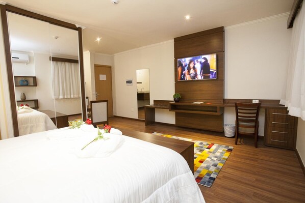 Una habitación de hotel con una cama grande, un escritorio, un televisor y un espejo.