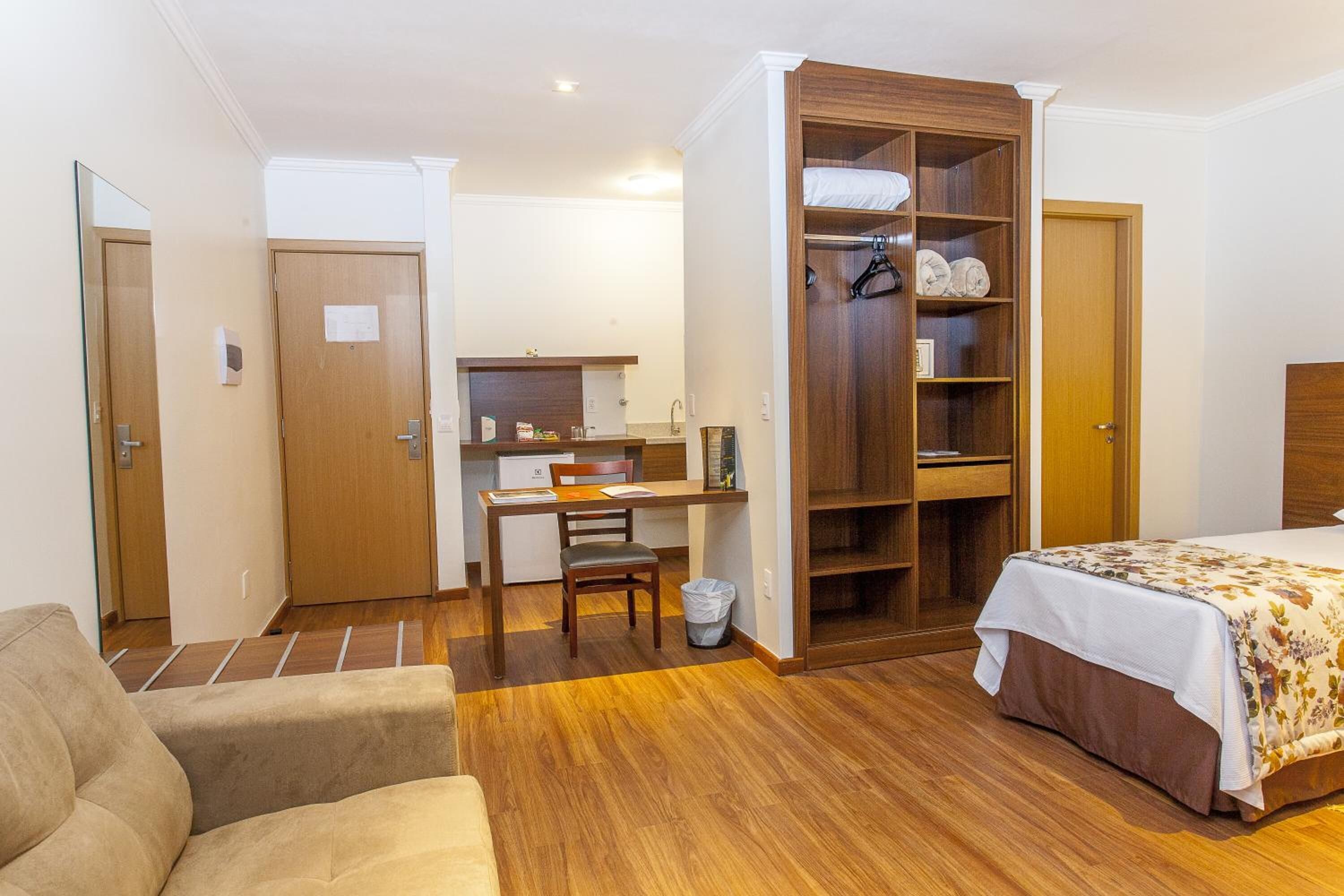 A bedroom with a bed, a wooden wardrobe, a desk, and a chair.