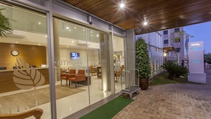 Uma área de recepção de hotel com portas de vidro, um balcão de atendimento e uma área de estar com cadeiras.