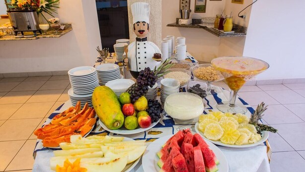 A buffet table with various fruits, a chef figurine, and a martini glass. - Costa do Rio Hotel (Petrolina)