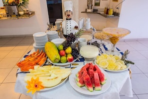 Una mesa de bufé con diversas frutas, una figurita de chef y una copa de martini.