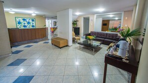 A hotel lobby with a reception desk, a sofa, a coffee table, and a mirror. - Costa do Rio Hotel (Petrolina)