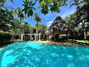 Una piscina rodeada de palmeras y una estructura con techo de paja.