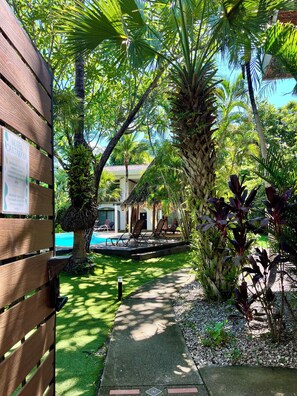 Un camino conduce a una zona de piscina con valla de madera y un cartel con el nombre del hotel.